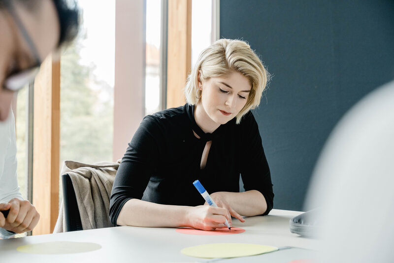 Studentin schreibt konzentriert auf Moderationskarte im Seminarraum der HOK