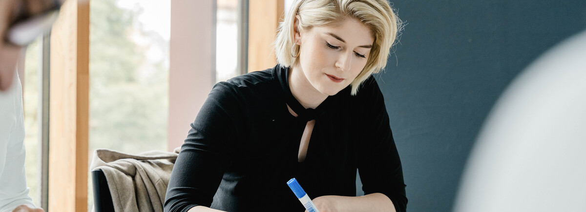 Studentin schreibt konzentriert auf Moderationskarte im Seminarraum der HOK