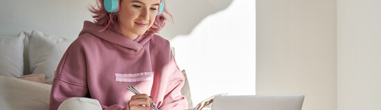 Studentin lernt mit Laptop, Notizbuch und Kopfhörern im Online-Unterricht von zuhause
