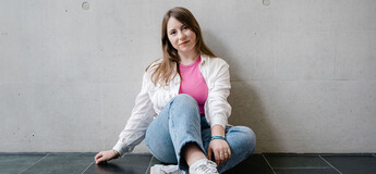 Studentin sitzt locker vor Betonwand am Campus der HOK.